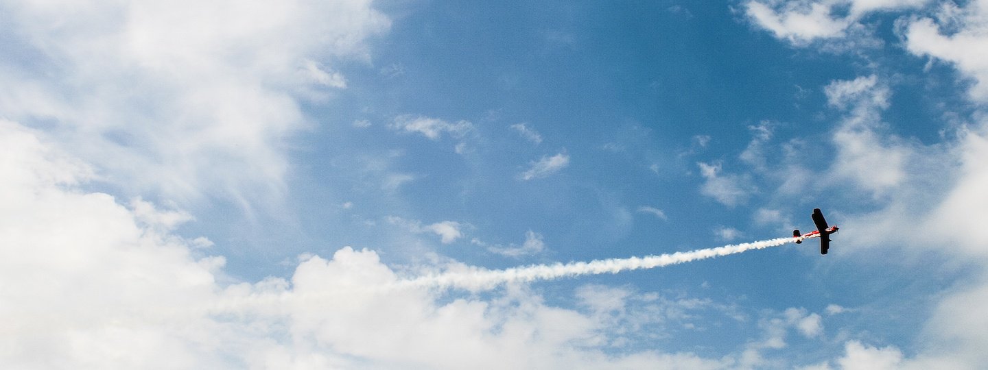 A small airplane leaves a trail of exhaust on a partly cloudy day