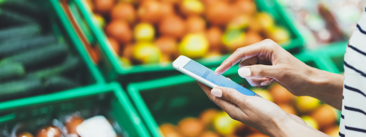A person on an iPhone in front of baskets of fruit and vegetables